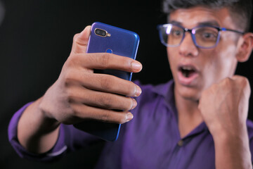 Smiling young man in glasses is using his phone to make a video call