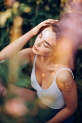 Young brunette in a tank top and shorts posing while sitting in the grass.