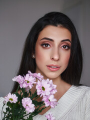 Fototapeta premium Magnificent portrait of a beautiful brunette young woman with perfect skin makeup closeup flowers bouquet