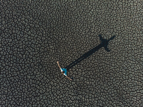 man creating cross shadow on dry lake