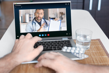 A close-up view of a patient's hand in front of a laptop during an online consultation with a doctor.