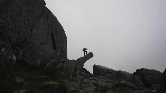 A man climbing onto a dangerous mountain ledge on Tryfan mountain in Snowdonia