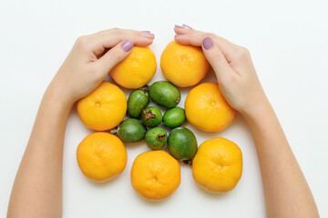 Female hands hold fresh tangerines and feijoaon white background. Froot flat lay top view