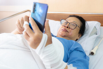 old woman patient using mobile phone in hospital bed