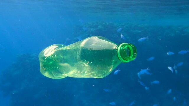 Plastic pollution, plastic bottle in blue water. Discarded green plastic bottle slowly drifting under surface of blue water near coral reef. Plastic garbage environmental pollution problem in Red Sea