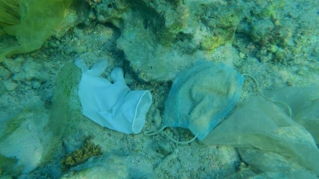 Close-up, Medical face mask and glove lies on the sebed. Coronavirus COVID-19 is contributing to pollution, as discarded used masks and gloves clutter polluting sea bottom along with plastic trash