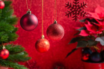 Red Christmas ball hanging against festive Christmas arrangement on red background. Selective focus.