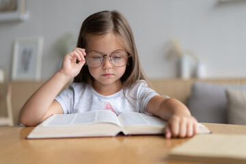 Portrait of happy small pupil learning at home. Smiling little child girl enjoying doing lessons in living room. Smart kid schoolgirl looking at camera