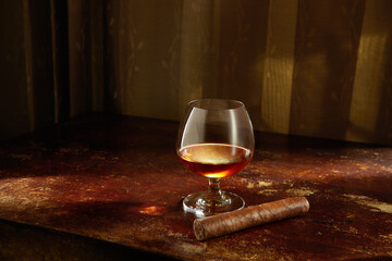Closed up view of glass of cognac with cigar aside on color back