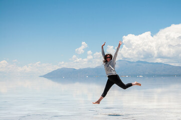 summer vacation woman happily jumping in the salt flats with blue sky, clouds and water