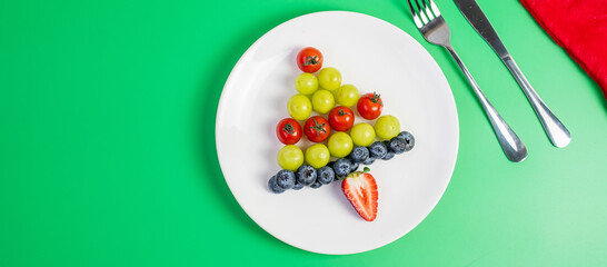Christmas tree of organic vegetable and fruit; Blueberries, grape, Strawberry and tomato with fork and knife on green background. Merry Xmas and happy New Year party, New You, Healthy food concept