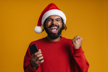 Excited african american guy using cellphone and making winner gesture