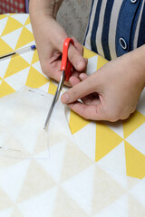 Women's hands cut the fabric with scissors according to the pattern on the table.