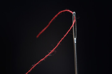 Needle and red thread on black background