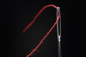 Needle and red thread on black background