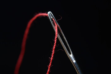 Needle and red thread on black background
