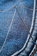 Close-up shot of needle with thread on jeans material. Close-up.
