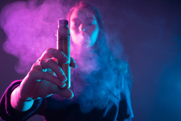 Vape. Vaper. Vaping. Woman holds out an electronic cigarette. Concept - girl gives a try a vape device. Concept - alternative to cigarettes. Smoking electronic cigarettes. Concept - vaper shop. E-cig