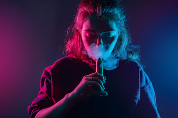 Woman smokes a vape. Girl with an e-cig at the mouth. Smoking with a vape device. Woman inhales the smoke of a cigarette. Concept - a store for vaping devices. Sale of electronic cigarettes. Student