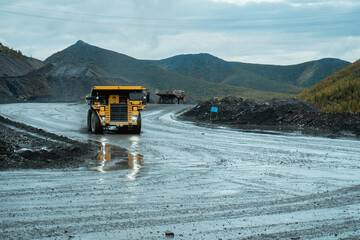 The mining dump truck drives on a dirty road at the gold mining site.