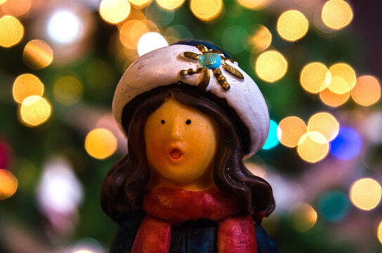 Figure of girl caroler in front of bokah lighted Christmas tree lights.