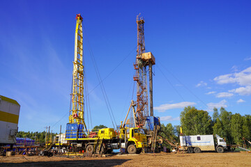 Fototapeta na wymiar In a row are oil-producing wells. In the background, work is underway to overhaul the well. Drilling rig for drilling oil and gas wells with various equipment and materials.