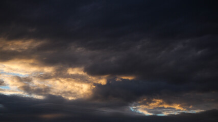 Naklejka na ściany i meble Ciel menaçant pendant le coucher du soleil. Les rayons du soleil viennent partiellement illuminer la base d'un gros cumulus
