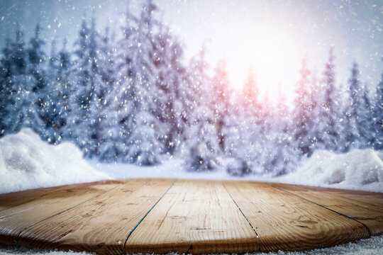 Snow on a wooden table surrounded by a beautiful winter setting sun with a landscape background