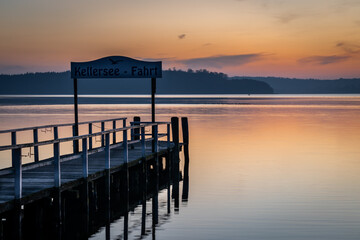 Fototapeta premium Jetty for ferry at Lake Kellersee with colorful sunset in autumn, Malente, Schleswig-Holstein