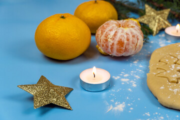 Gingerbread cookies in the form of fir trees on raw dough, fir branches, tangerines, candles and small gifts on a blue background.