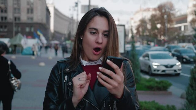 Shocked woman holding smartphone of the blurred city background 4k