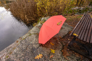 Red umbrella. A beautiful large bright red umbrella lies on the shore of the lake. Autumn landscape on a cloudy rainy day. Lake shores. Forgotten umbrella at the waters edge.