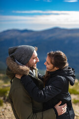 Young couple in love and in winter clothes hug and smile in front of the mountain range in a sunny day