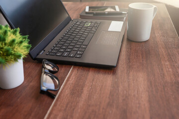 Laptop, mug, eyeglasses, smartphone, and notebook on wooden table