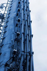 Fragment of high metal pipe with cable routes, antennas and steps against cloudy sky background.