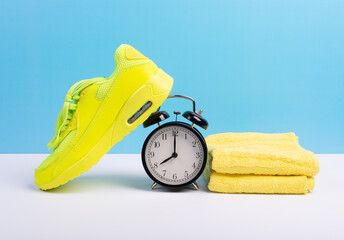 Marathon running concept with sport shoe, towel and alarm clock over blue wall background