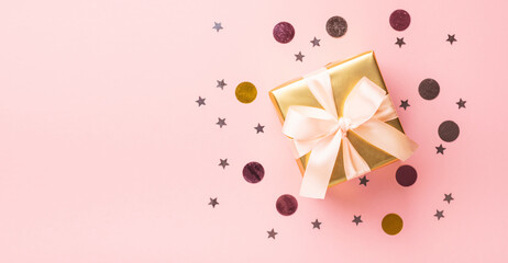 Festive box with a shiny ribbon bow pastel pink background sequins confetti.