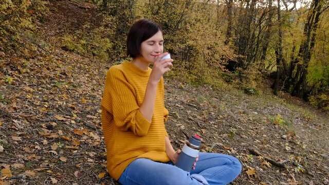 Pretty young woman with hot tasty drink spending vacations among autumn forest. Traveling in mountains wilderness. Wanderlust and hipster style