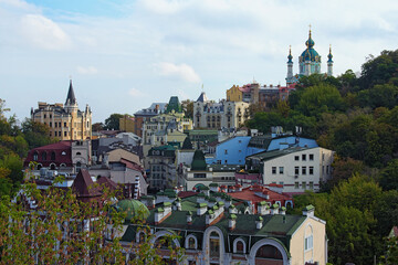 Picturesque morning landscape view of ancient buildings of Andrew's Descent (Andriyivsky uzviz, Podil neighborhood) and Saint Andrew's Church on the top of the hill. Blue sky at the background. Kyiv