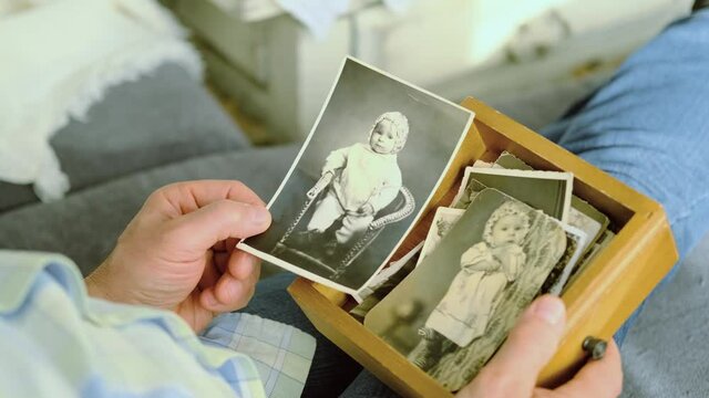 an elderly man looks through his old photographs of 1960-1965, the concept of nostalgia and memories of youth, childhood, remembering his life, relatives, family connection of generations