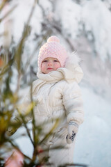 Little girl toddler in warm clothes walks in the winter forest against the background of New Year's decorations

