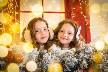 Fototapeta na wymiar two red-haired sisters on the veranda of a house decorated for Christmas. garland lights, bokeh