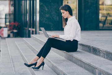 Full length photo of cute pretty young lady dressed white formal shirt high-heels typing modern gadget sitting stairs outside