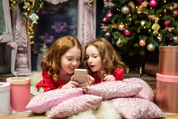 two red-haired sisters near the New Year trees, looking at the phone. Christmas, gadgets, online