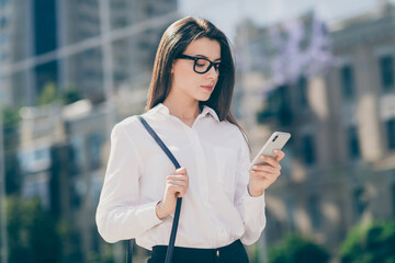 Photo of adorable young lady dressed white formal shirt glasses handbag looking writing modern device outside