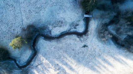Aerial view of meandering river on snow covered ground. White fields with curved brook flowing...