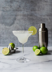 Close up of margarita cocktail with limes and shaker on marble counter