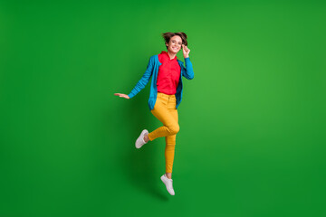 Full length body size photo of cheerful girl jumping smiling touching eyewear in colorful clothes isolated on bright green color background