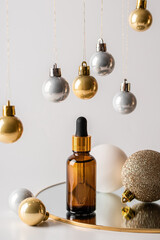 Christmas minimalistic composition with brown glass serum bottle on the mirror and hanging golden balls. Health and beauty concept.