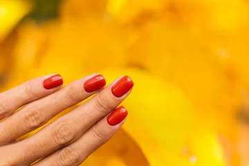 Close outdoor shot of womans hands in park orange color manicure, autumn mood. 